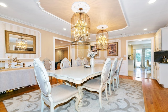 dining area with a wainscoted wall, a tray ceiling, crown molding, light wood finished floors, and a chandelier