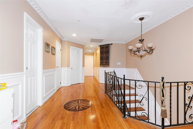 hallway with crown molding, a wainscoted wall, an upstairs landing, an inviting chandelier, and light wood-style floors