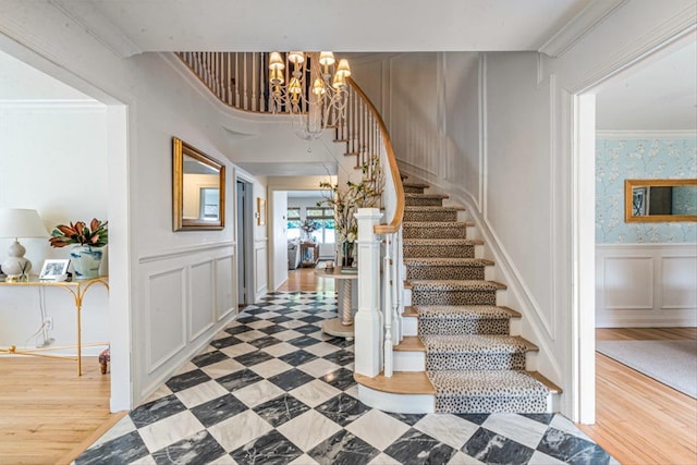 entrance foyer featuring wallpapered walls, crown molding, stairs, wainscoting, and a decorative wall