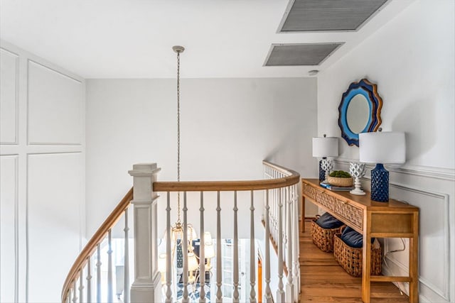 hall featuring an upstairs landing, visible vents, a decorative wall, and wood finished floors