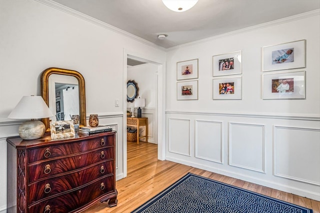 bedroom with a wainscoted wall, a decorative wall, light wood-type flooring, and ornamental molding