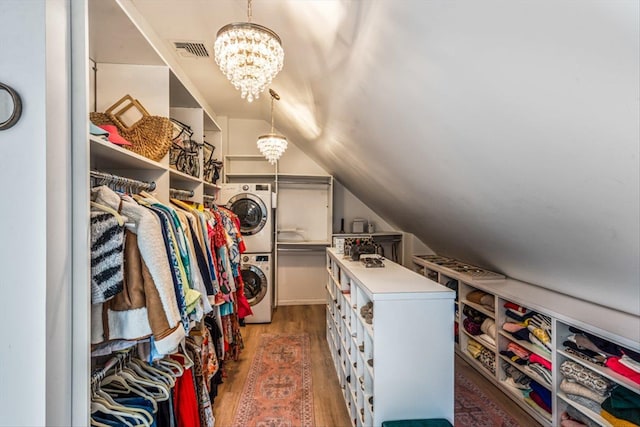 walk in closet with visible vents, wood finished floors, an inviting chandelier, stacked washer / dryer, and lofted ceiling