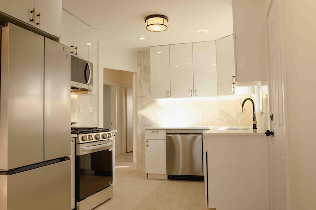 kitchen featuring backsplash, light countertops, appliances with stainless steel finishes, white cabinets, and a sink