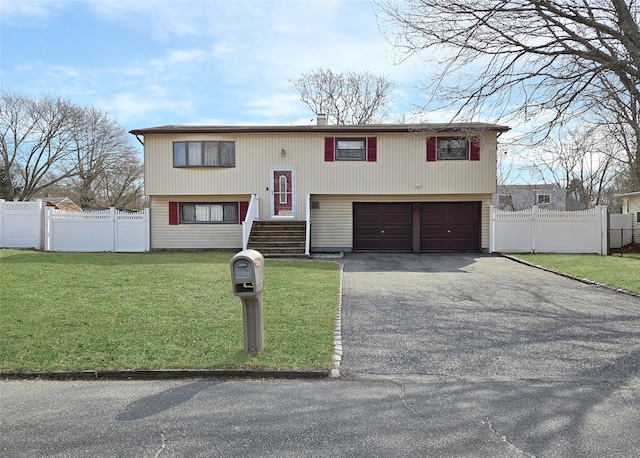 bi-level home featuring driveway, an attached garage, a front yard, and fence