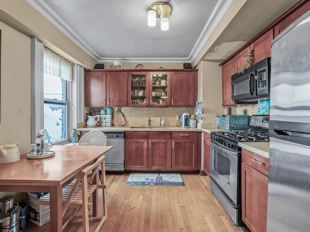 kitchen with light wood finished floors, a sink, ornamental molding, light countertops, and stainless steel appliances