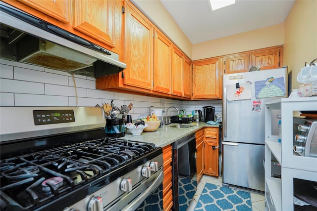 kitchen featuring under cabinet range hood, a sink, backsplash, appliances with stainless steel finishes, and light stone countertops