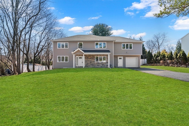 view of front of property featuring a front lawn, driveway, stone siding, fence, and an attached garage