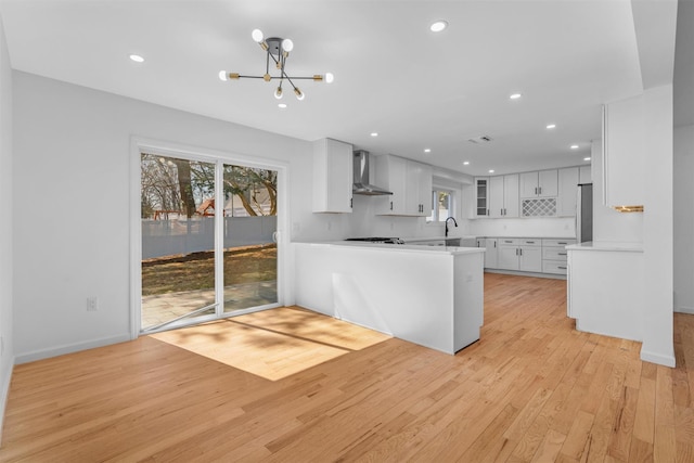 kitchen with a sink, light countertops, wall chimney exhaust hood, a notable chandelier, and light wood-type flooring