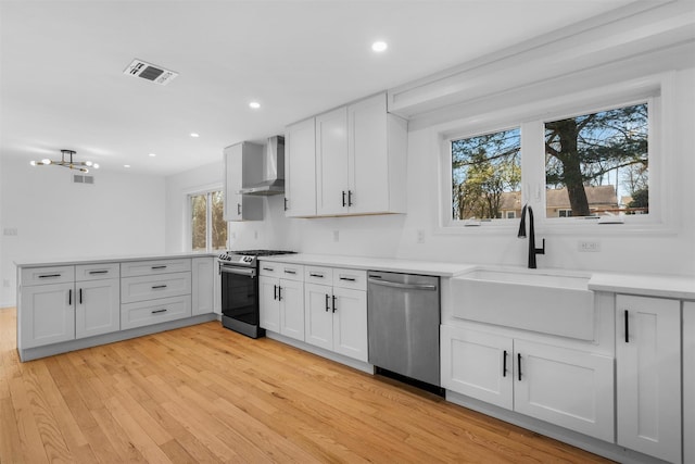 kitchen featuring visible vents, a peninsula, a sink, stainless steel appliances, and wall chimney exhaust hood