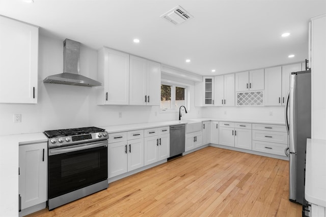 kitchen featuring visible vents, wall chimney range hood, light wood-style floors, white cabinets, and stainless steel appliances