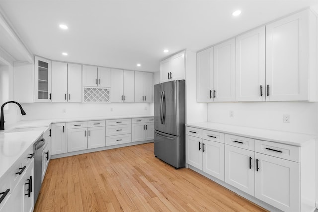 kitchen featuring a sink, white cabinetry, stainless steel appliances, light wood finished floors, and glass insert cabinets