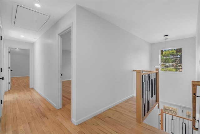 corridor with an upstairs landing, light wood-style flooring, attic access, and baseboards