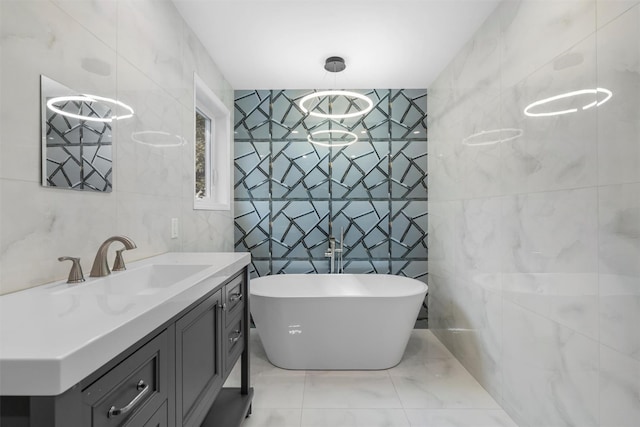 bathroom featuring marble finish floor, tile walls, vanity, and a freestanding tub