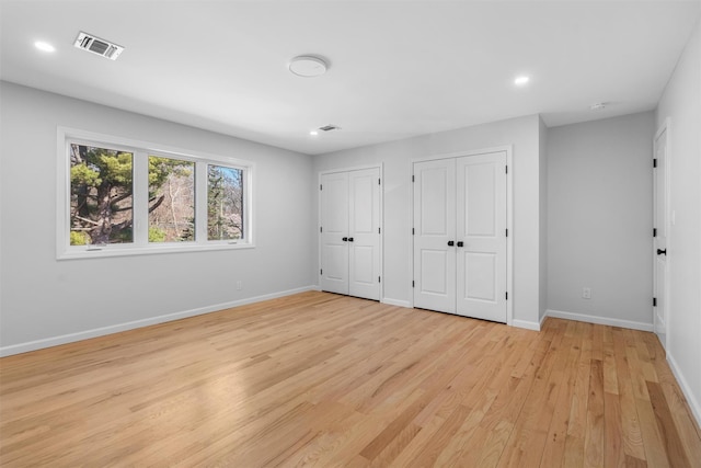 unfurnished bedroom featuring visible vents, two closets, baseboards, recessed lighting, and light wood-style flooring