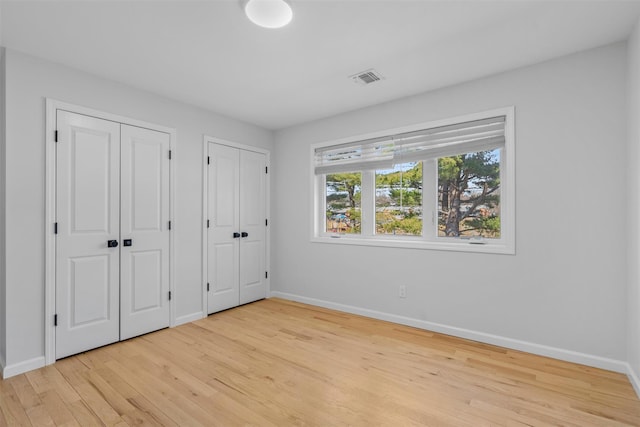 unfurnished bedroom featuring baseboards, visible vents, two closets, and light wood-type flooring