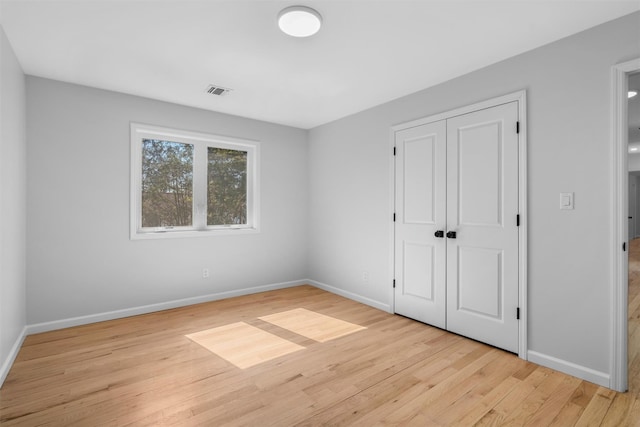 unfurnished bedroom featuring a closet, baseboards, visible vents, and light wood finished floors