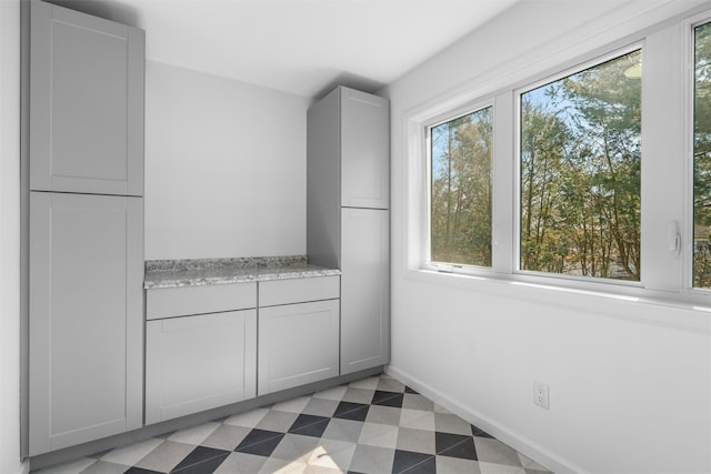 interior space with baseboards, light floors, gray cabinets, and light stone countertops