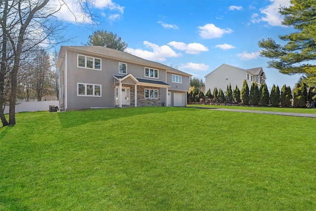 view of front of home with driveway, a front lawn, stone siding, fence, and a garage