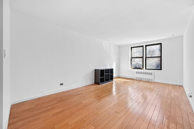 unfurnished living room featuring baseboards, radiator heating unit, and light wood finished floors