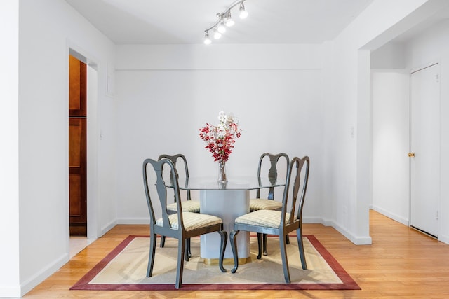 dining space featuring light wood-type flooring, baseboards, and rail lighting