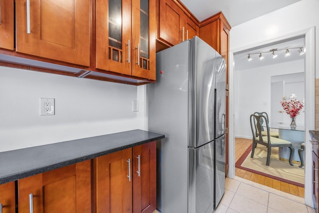 kitchen with light tile patterned floors, glass insert cabinets, brown cabinets, and freestanding refrigerator