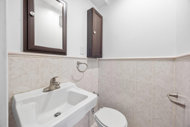 bathroom with tile walls, toilet, a wainscoted wall, and a sink