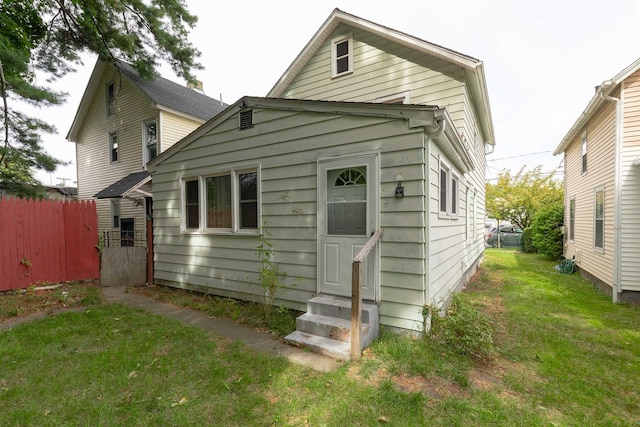 rear view of house with a lawn, entry steps, and fence