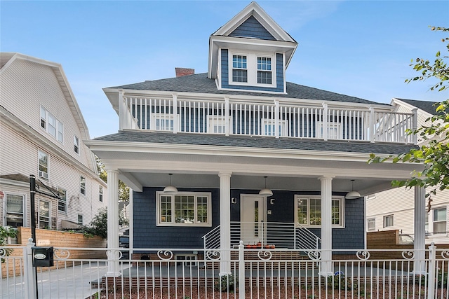 view of front facade featuring a fenced front yard, a balcony, a porch, and roof with shingles