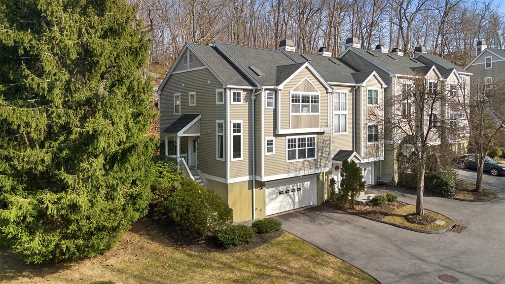 exterior space with an attached garage, a residential view, driveway, and a shingled roof