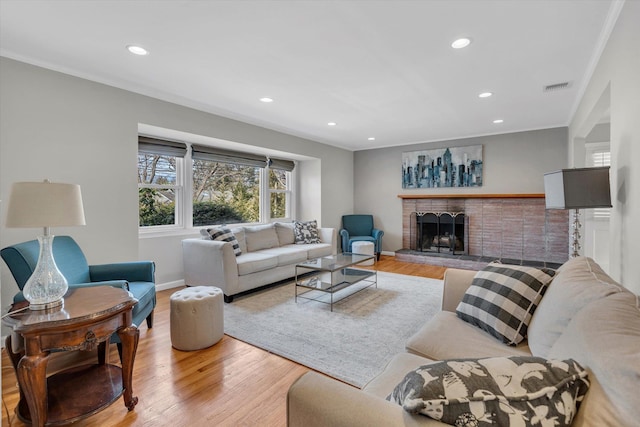 living area featuring visible vents, crown molding, recessed lighting, a fireplace, and wood finished floors