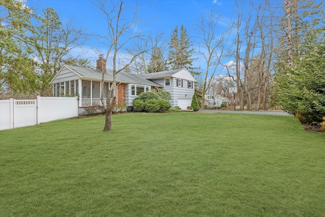 view of front of house with fence, an attached garage, a sunroom, a chimney, and a front lawn