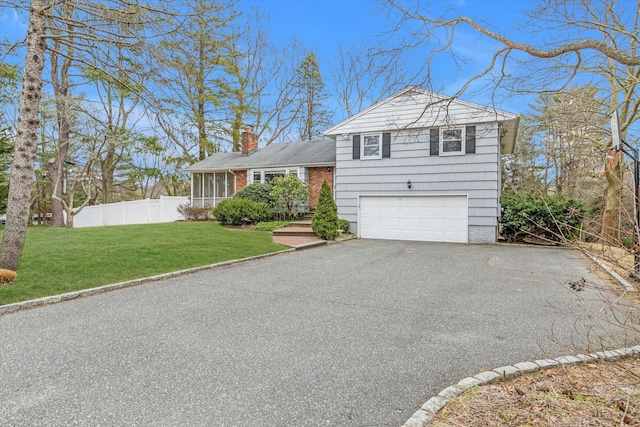 split level home with fence, driveway, an attached garage, a chimney, and a front lawn