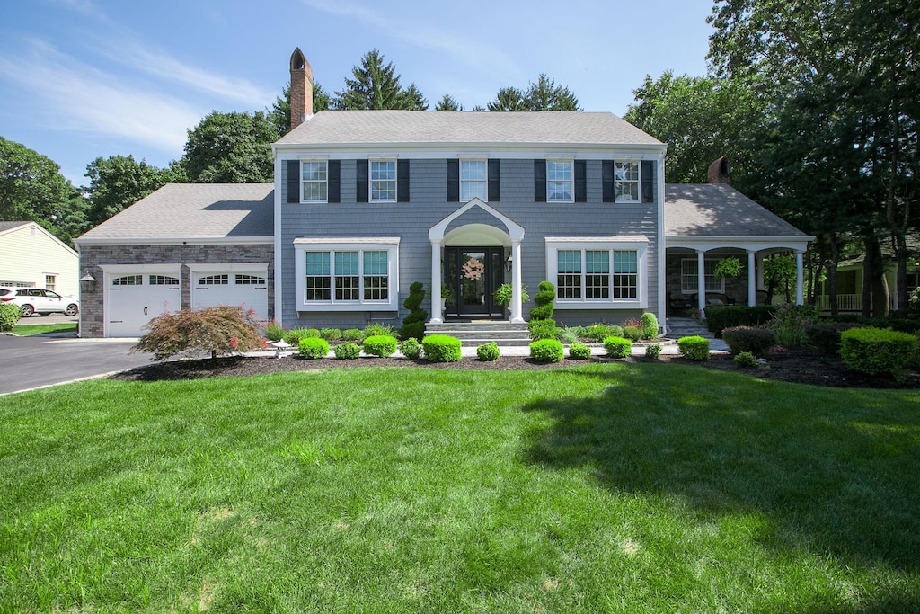 colonial inspired home featuring a garage, a front lawn, a chimney, and aphalt driveway