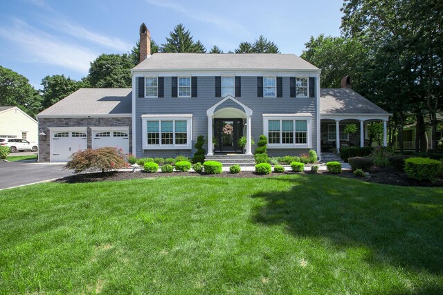 colonial inspired home with a garage, a front lawn, a chimney, and aphalt driveway