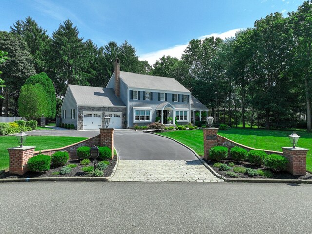 view of front of property featuring a front yard, an attached garage, a chimney, stone siding, and aphalt driveway