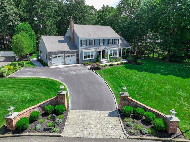 colonial house with aphalt driveway, a chimney, a garage, and a front yard