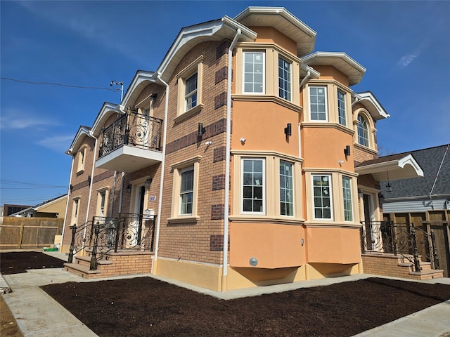 view of property exterior with brick siding, stucco siding, a balcony, and fence