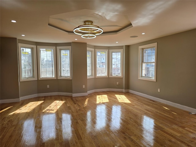 spare room with wood finished floors, baseboards, an inviting chandelier, recessed lighting, and a raised ceiling