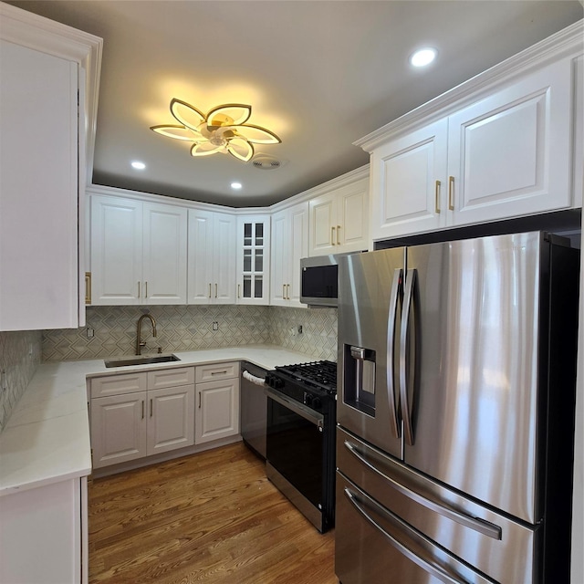 kitchen with a sink, wood finished floors, white cabinetry, and stainless steel appliances