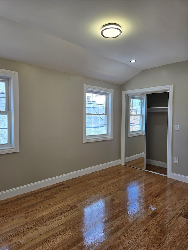 unfurnished bedroom with a closet, lofted ceiling, baseboards, and wood finished floors