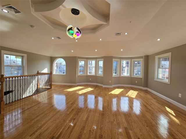 empty room with visible vents, light wood-style flooring, baseboards, and a tray ceiling