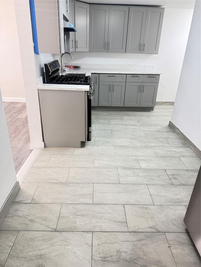 kitchen featuring under cabinet range hood, gas range, gray cabinets, and light countertops