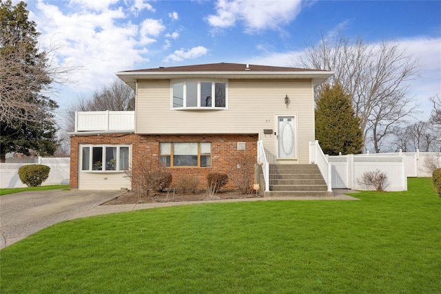 view of front of home featuring brick siding, driveway, a front lawn, and fence