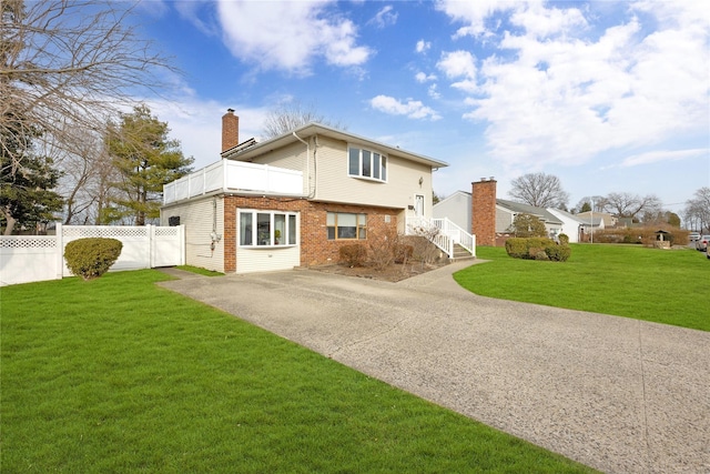 view of side of property featuring fence, driveway, a chimney, a lawn, and brick siding