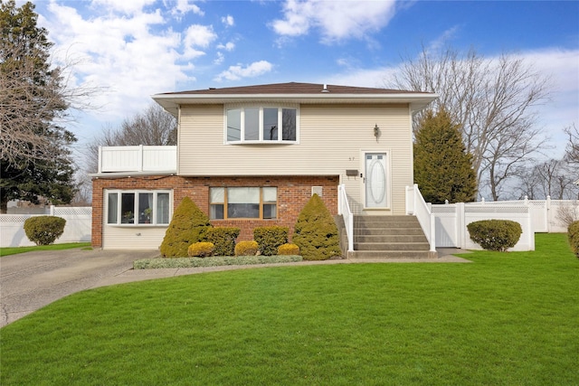 view of front of house with a front yard, fence, brick siding, and driveway