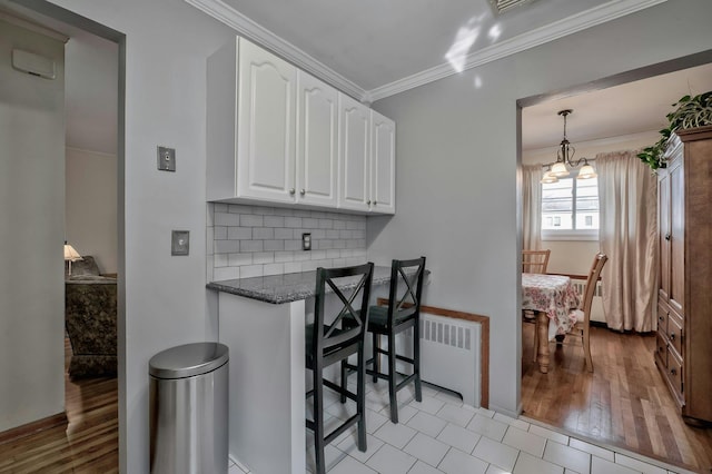 kitchen with tasteful backsplash, radiator, crown molding, a chandelier, and white cabinets