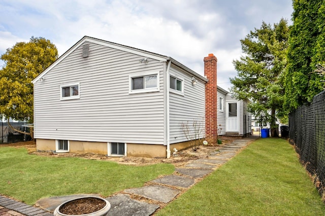 view of side of home featuring fence, entry steps, an outdoor fire pit, a lawn, and a chimney