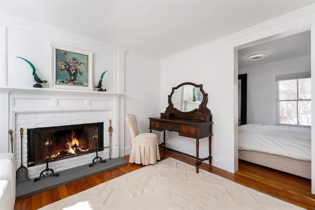 living area with crown molding, a brick fireplace, wood finished floors, and baseboards