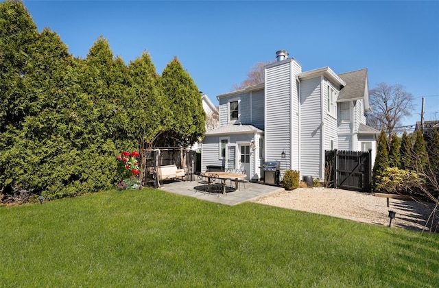 back of house featuring a gate, fence, a chimney, a patio area, and a lawn