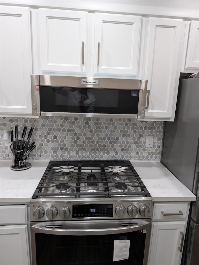 kitchen with stainless steel appliances, light stone countertops, tasteful backsplash, and white cabinetry